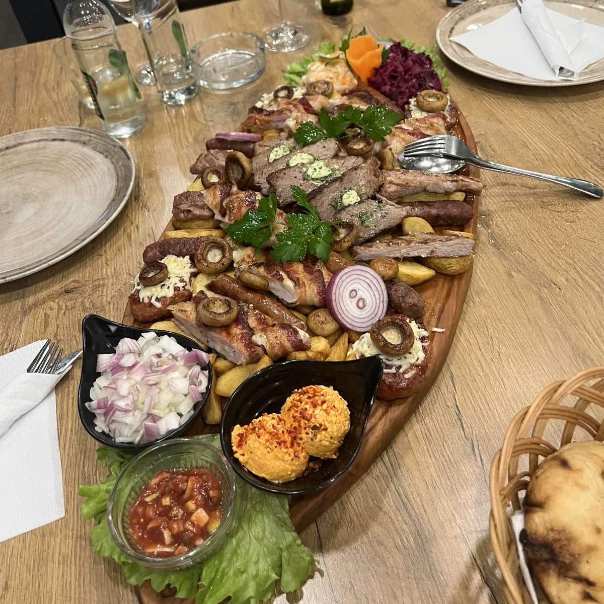 Duga daska sa mješanim mesom sa roštilja i prilozima na postavljenom stolu